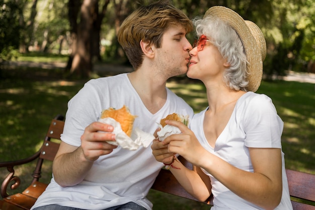 Joven pareja besándose mientras disfruta de hamburguesas en el parque