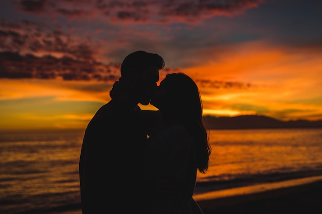 Joven pareja besándose en la orilla del mar en la noche