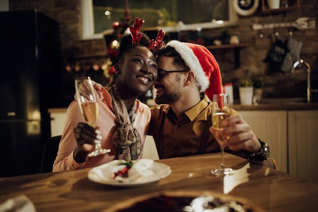 Joven pareja cariñosa bebiendo champán en la mesa de comedor en Nochebuena