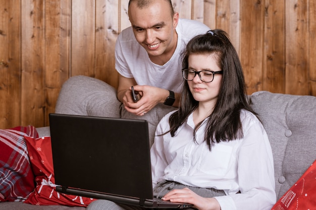 Una joven pareja en casa sentada en el sofá comunicándose en línea a través de una computadora portátil con familiares