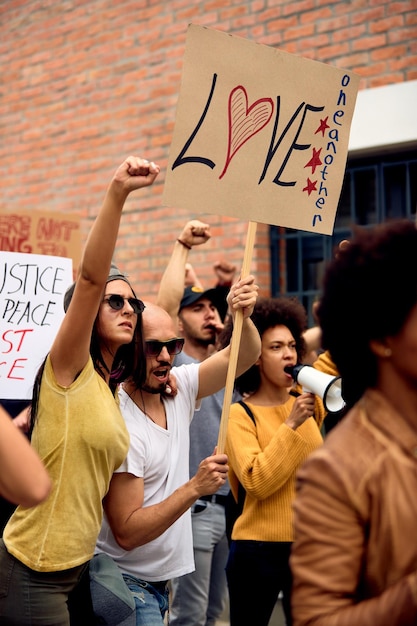 Joven pareja caucásica protestando con un grupo de personas contra el racismo y llevando una pancarta con inscripción de amor mutuo
