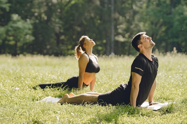 Joven pareja deportiva haciendo yoga fitness. Personas en un parque de verano.