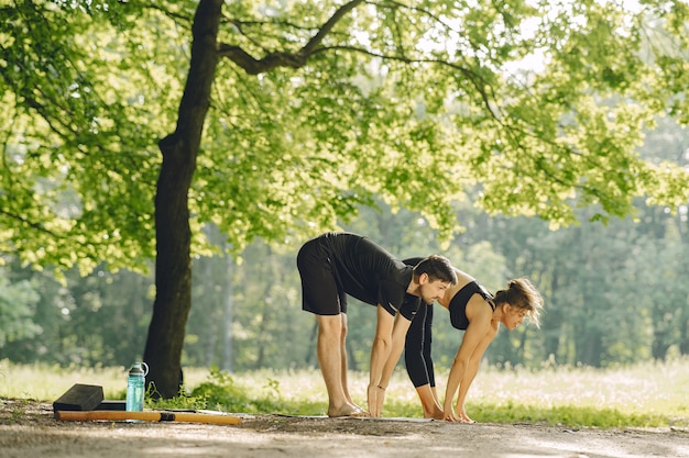 Joven pareja deportiva haciendo yoga fitness. Personas en un parque de verano.