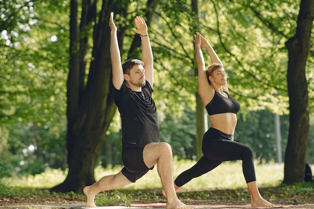 Joven pareja deportiva haciendo yoga fitness. Personas en un parque de verano.