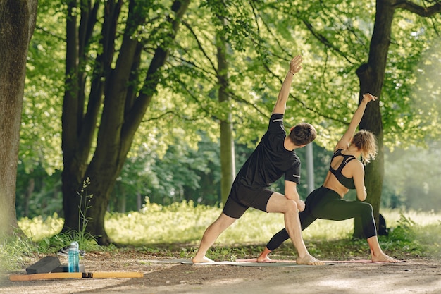 Joven pareja deportiva haciendo yoga fitness. Personas en un parque de verano.