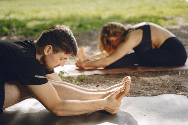 Joven pareja deportiva haciendo yoga fitness. Personas en un parque de verano.