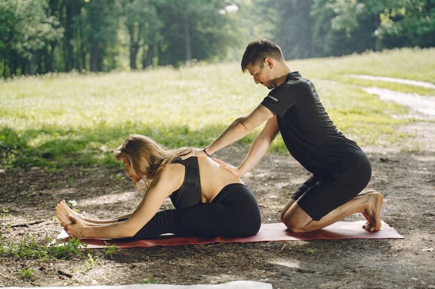 Joven pareja deportiva haciendo yoga fitness. Personas en un parque de verano.