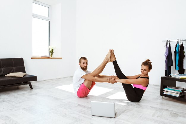 Joven pareja deportiva hermosa practicando asanas de yoga en casa. Navasana