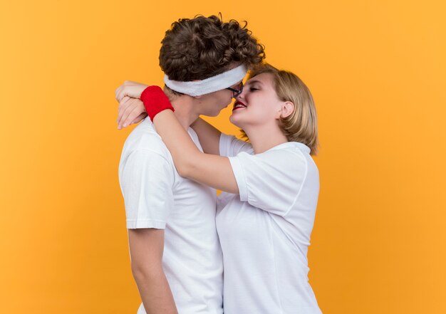 Joven pareja deportiva hombre y mujer abrazándose y besándose feliz en el amor de pie sobre la pared ornge