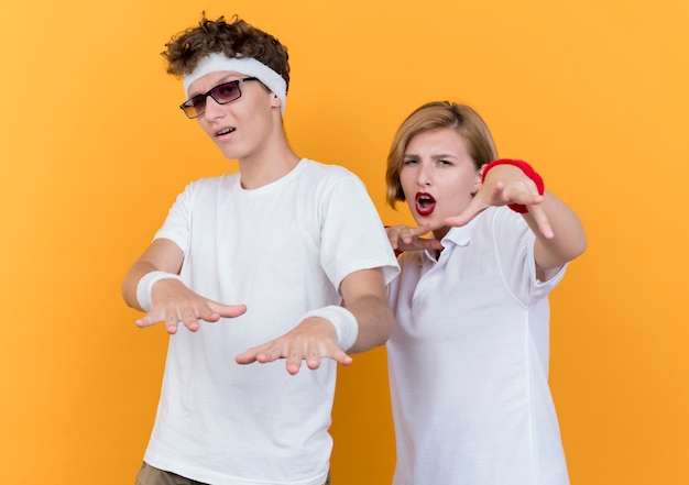 Joven pareja deportiva hombre y mujer con manos sonriendo divirtiéndose de pie sobre la pared naranja