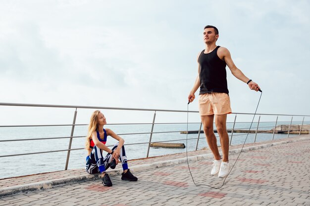 Joven pareja deportiva trabajando juntos en el muelle, cerca del mar.