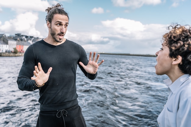 Joven pareja discutiendo expresivamente con el mar desenfocado