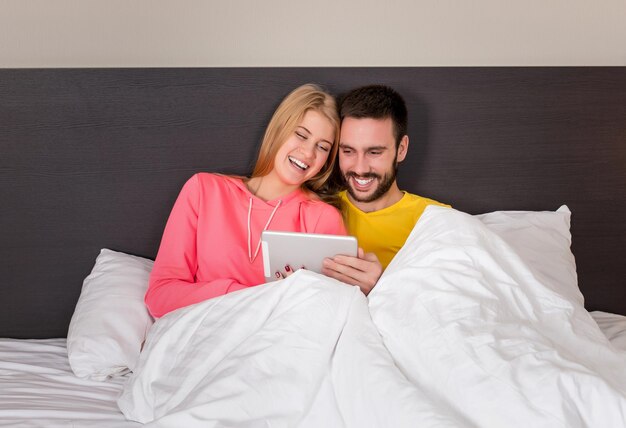 Joven pareja dulce en la cama viendo algo en el gadget de la tableta. Concepto sobre tecnología y personas.