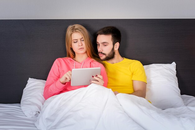 Joven pareja dulce en la cama viendo algo en el gadget de la tableta. Concepto sobre tecnología y personas.