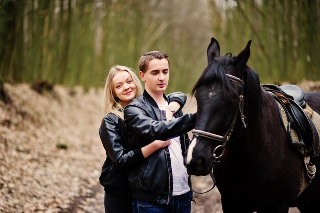 Joven pareja elegante en el amor cerca de caballo en el bosque de otoño