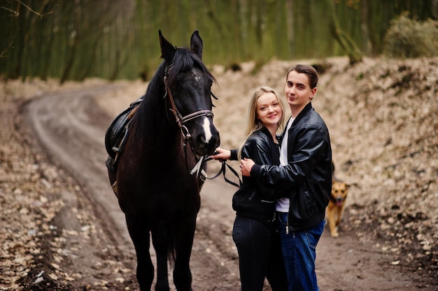 Joven pareja elegante en el amor cerca de caballo en el bosque de otoño