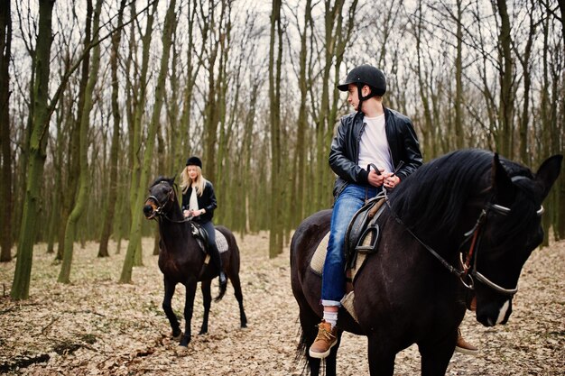 Joven pareja elegante montando a caballo en el bosque de otoño