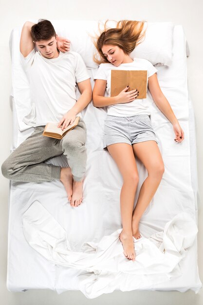 La joven pareja encantadora acostada en una cama con libros