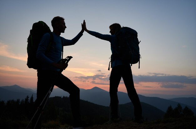 Joven pareja de excursionistas chocando los cinco durante la puesta de sol en las montañas