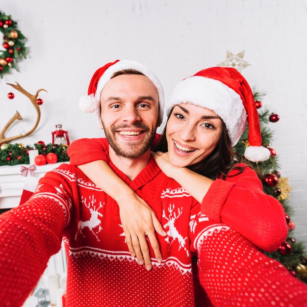 Joven pareja feliz abrazando en sombreros de la Navidad