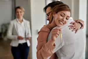 Foto gratuita joven pareja feliz abrazándose mientras compra su primera casa el foco está en la mujer que sostiene las llaves de la nueva casa