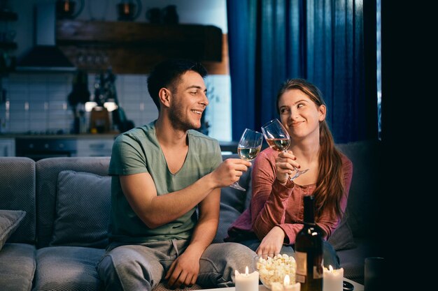 Joven pareja feliz brindando con vino por la noche en casa