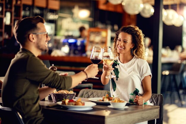 Joven pareja feliz celebrando y brindando con copas de vino mientras come en un restaurante