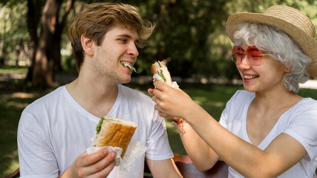 Joven pareja feliz comiendo hamburguesas en el parque