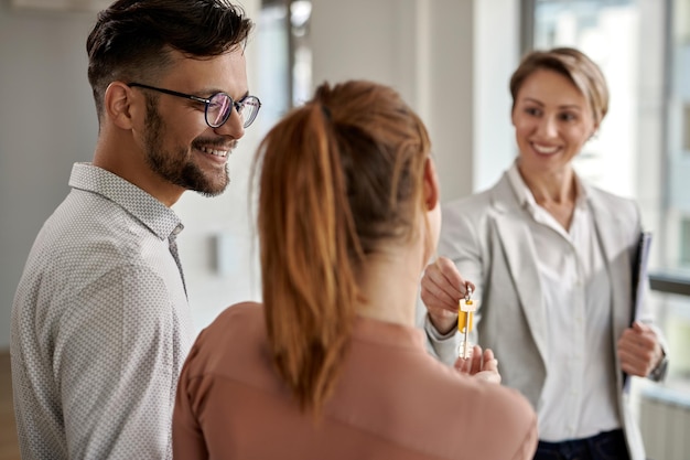 Joven pareja feliz comprando una casa nueva y recibiendo la llave de su agente inmobiliario