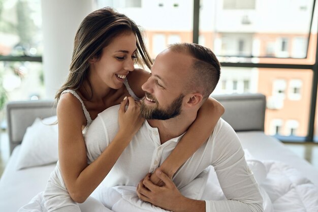 Una joven pareja feliz hablando mientras se sienta abrazada en una cama