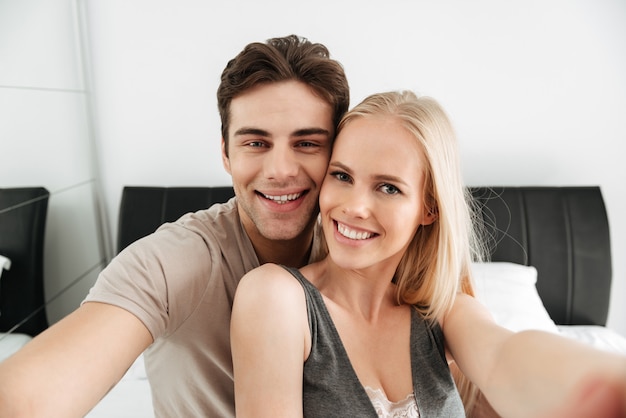 Joven pareja feliz haciendo selfie mientras está acostado en la cama