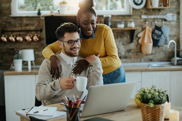 Joven pareja feliz leyendo un correo electrónico en la computadora portátil en casa