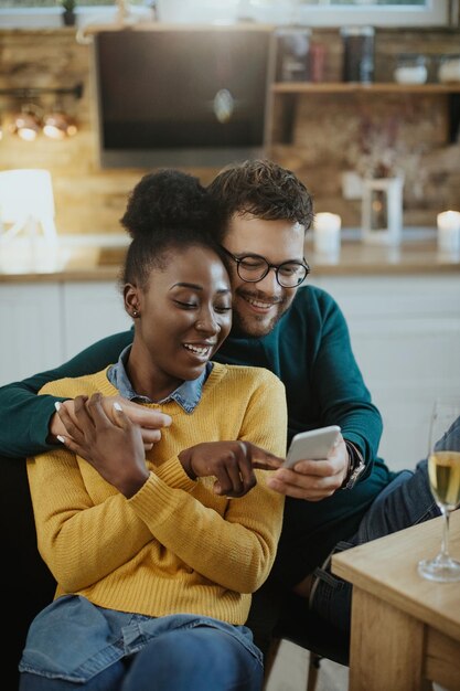 Joven pareja feliz mensajes de texto en el teléfono celular en casa