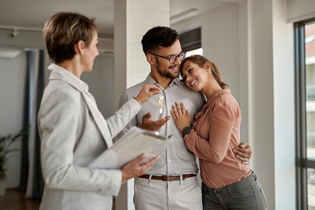 Joven pareja feliz recibiendo llaves de su nuevo hogar de un agente inmobiliario