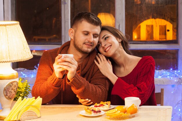 La joven pareja feliz con tazas de té y pasteles.