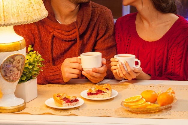 La joven pareja feliz con tazas de té y pasteles.