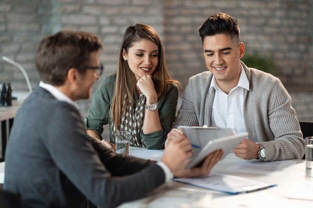 Una joven pareja feliz teniendo consultas con el gerente del banco en una reunión en la oficina
