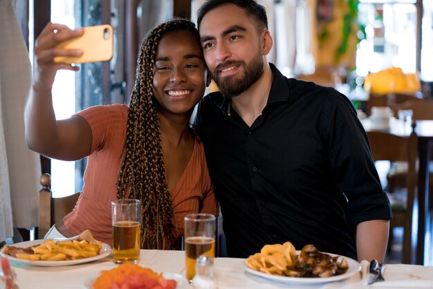 Joven pareja feliz tomando un selfie con un teléfono móvil mientras disfruta de una cita en un restaurante.