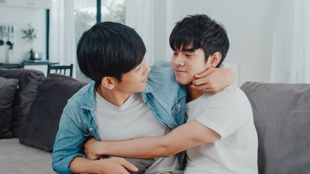 Joven pareja gay asiática abrazo y beso en casa. Los hombres de orgullo LGBTQ asiáticos y felices se relajan felices y pasan un momento romántico juntos mientras descansan en el sofá de la sala.