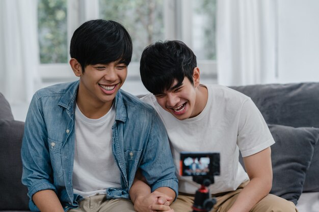 Joven pareja gay asiática influyente pareja vlog en casa. Adolescentes coreanos LGBTQ hombres felices relajarse diversión usando cámara grabar vlog video subir en las redes sociales mientras está acostado sofá en la sala de estar en casa.