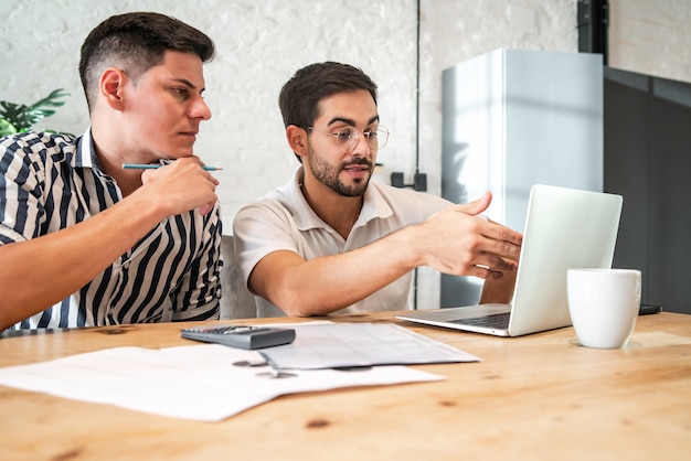 Foto gratuita joven pareja gay planeando el presupuesto de su casa y pagando sus facturas en línea con una computadora portátil mientras se queda en casa. concepto de finanzas.