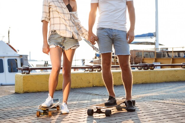 Joven pareja hermosa caminando en la playa, el skate. Cerca de las piernas.