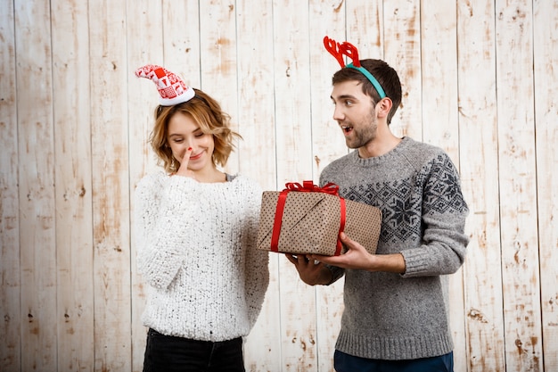 Joven pareja hermosa celebración de regalo de Navidad sobre pared de madera