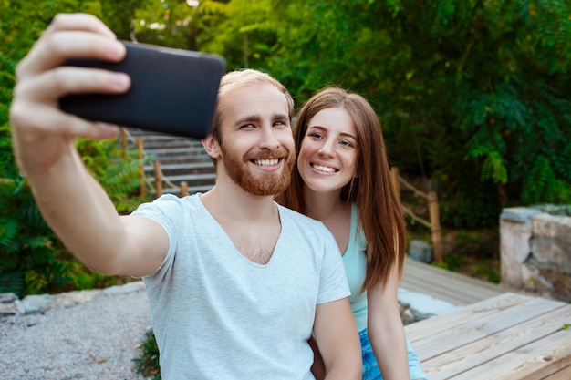 Joven pareja hermosa haciendo selfie, sonriendo, caminando en el parque