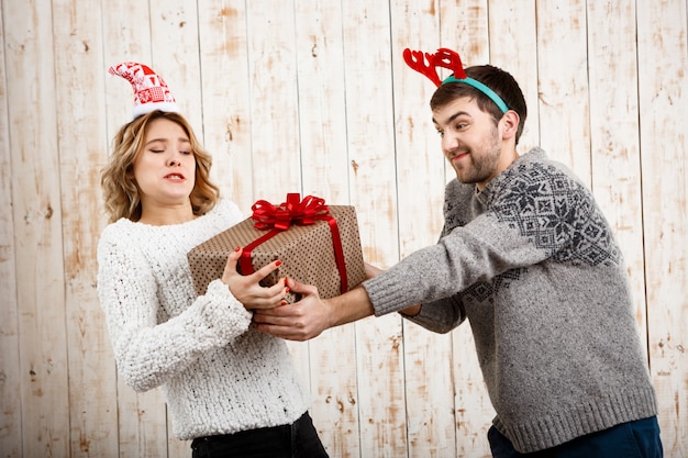 Joven pareja hermosa luchando por el regalo de Navidad sobre pared de madera