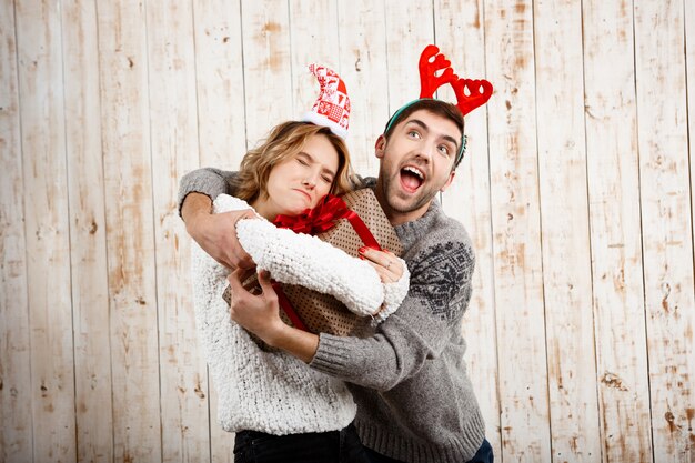 Joven pareja hermosa luchando por el regalo de Navidad sobre pared de madera