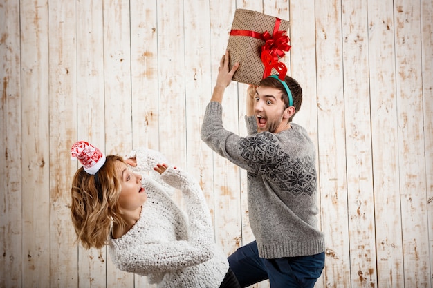 Joven pareja hermosa luchando por el regalo de Navidad sobre superficie de madera