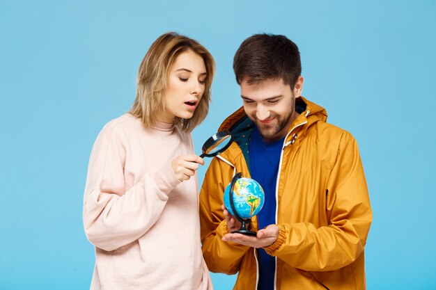 Joven pareja hermosa posando sobre pared azul con lupa y globo terráqueo