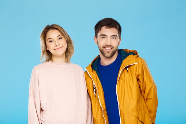 Foto gratuita joven pareja hermosa posando sonriendo divirtiéndose sobre pared azul hombre con abrigo de lluvia.