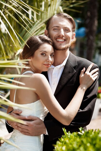 Joven pareja hermosa de recién casados sonriendo, abrazándose en el parque.